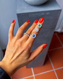 Hand wearing multiple rings with gemstones on a neutral background