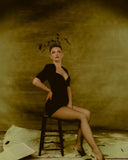 Woman in a black dress sitting on a stool against a textured wall. Cero magazine Mara Megelea