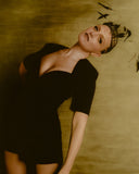 Woman in a black dress against a textured beige wall. Cero Magazine. Mara Megelea