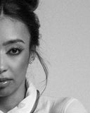 Black and white close-up of a person with hair styled in an updo against a plain background. Diamond earrings. Mara Megelea