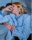 Person wearing a blue and white checkered outfit with a colorful scarf, sitting on a couch. Mara Megelea Prestige Magazine